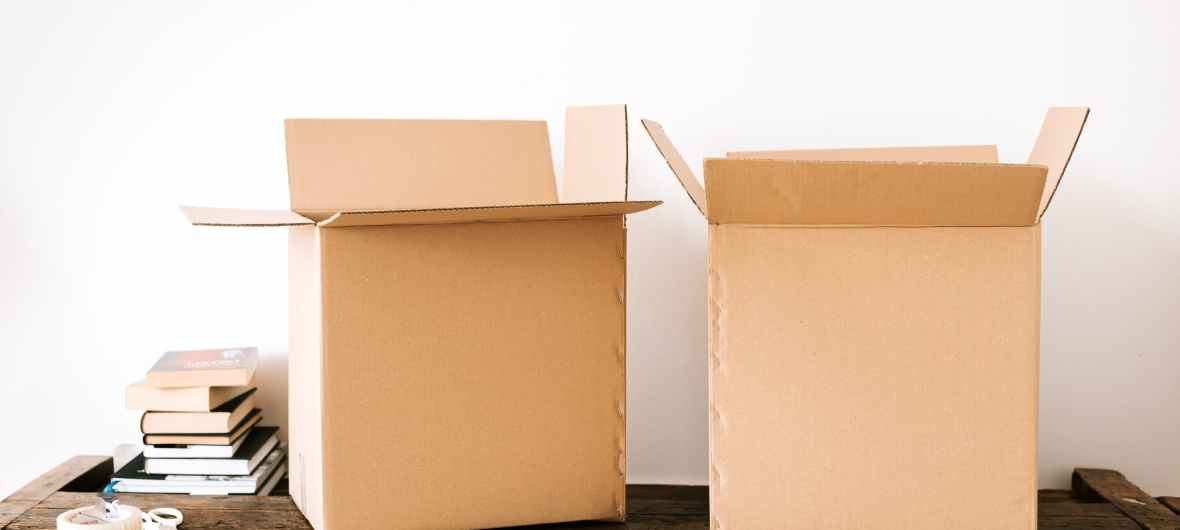 Two open, empty shipping boxes stand on a table with books and tape