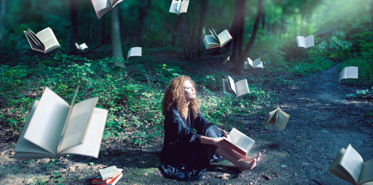 A young redheaded woman sits dreamily in a lush forest clearing, sunlight cascading across her face. Open books float in the air all around her, and she holds one loosely propped against her bare feet.