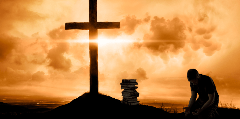 A man kneels at the cross, silhouetted by a cloudy sunset. He palms are open, his head bowed, and a stack of books rests at the foot of the cross.